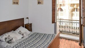 Una camera da letto con un letto, un comodino, una lampada e un balcone con vista su un edificio.