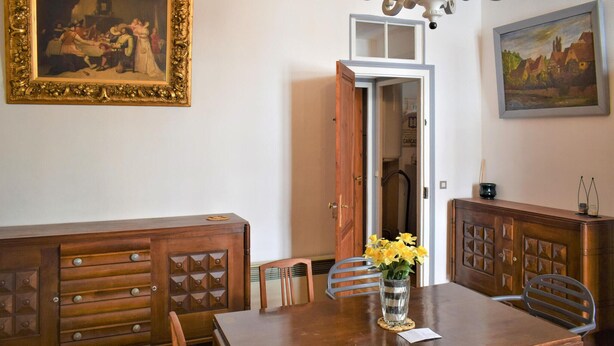 Zona pranzo con tavolo di legno, sedie, un vaso con fiori, un armadietto e due quadri alle pareti.