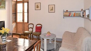 Una camera accogliente con un tavolo da pranzo in legno, due sedie, un tavolino rotondo con un oggetto decorativo, un divano e una libreria piena di libri.