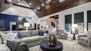 Ein geräumiges Wohnzimmer mit einem grauen Ecksofa, gemusterten Sessel und einem schwarzen Couchtisch.