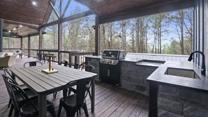 Eine überdachte Terrasse mit Esstisch, Stühlen, Grill und Spüle.
