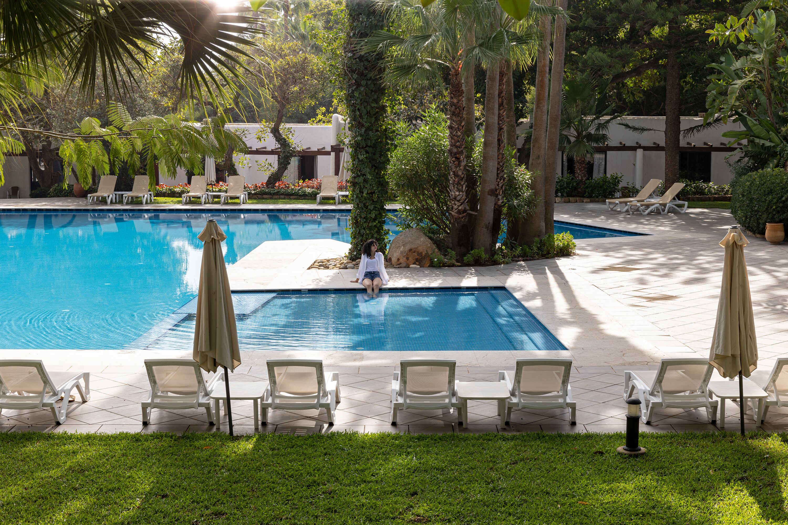 A pool area with multiple lounge chairs and umbrellas, surrounded by lush greenery.