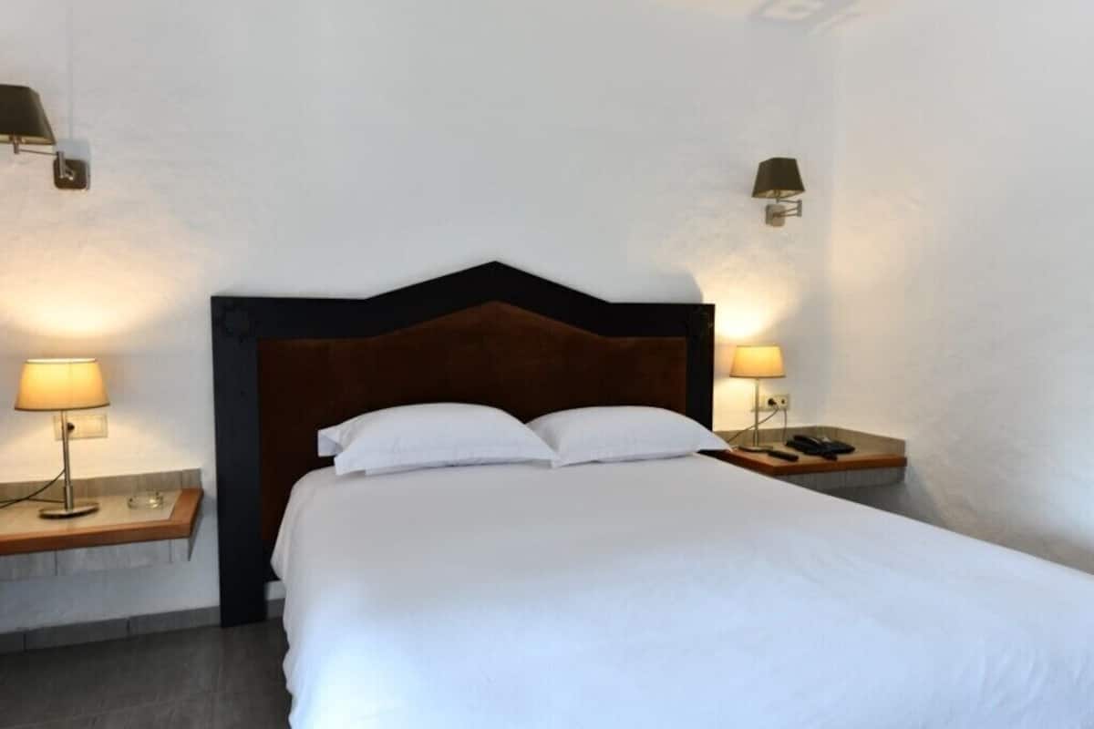 A hotel room with a large bed, two bedside tables with lamps, and a wooden headboard.