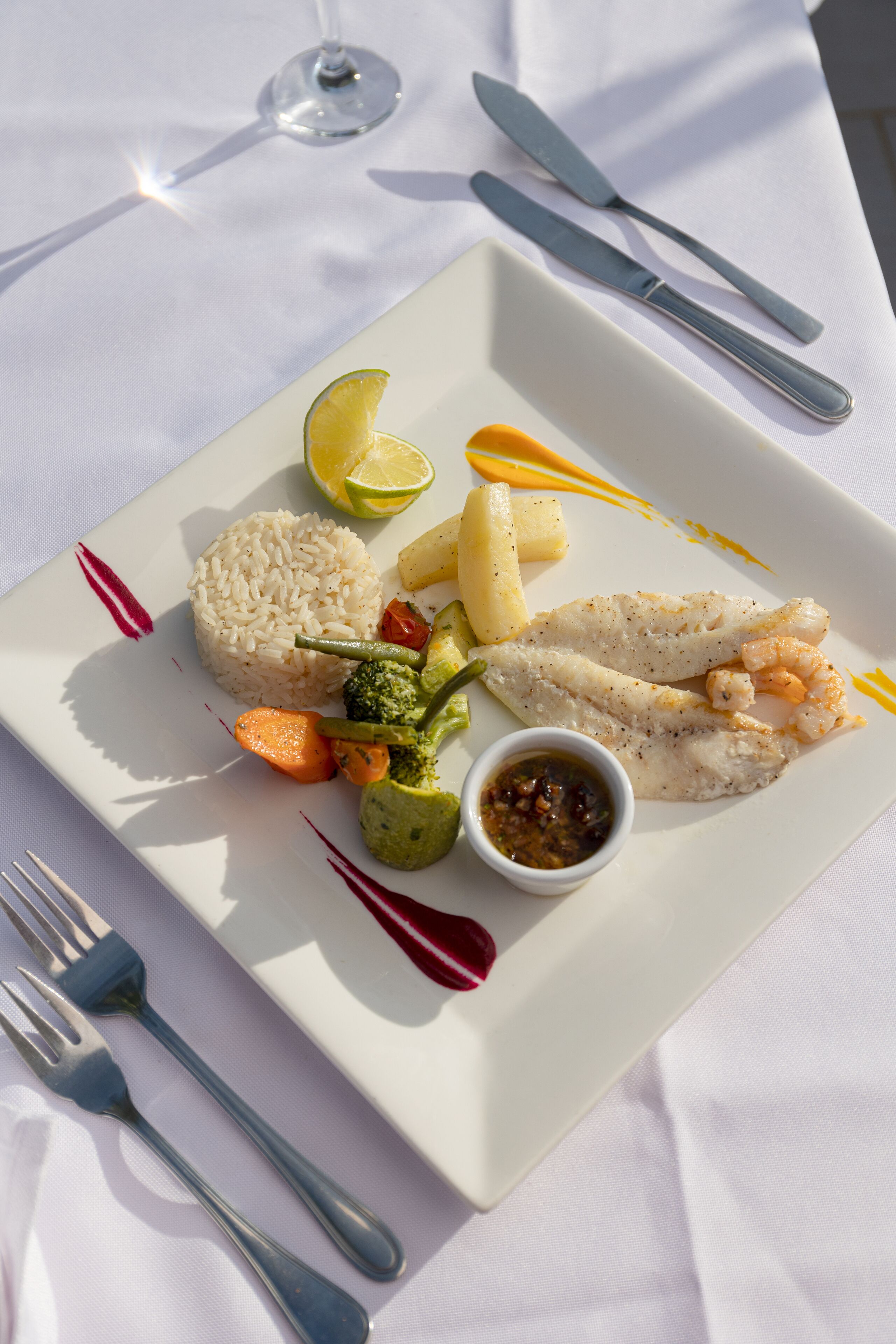 Un plato blanco con arroz, pescado, verduras y un gajo de limón.