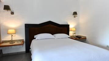 A neatly made bed with white linens, two bedside lamps, and a wooden nightstand with a phone and remote control.