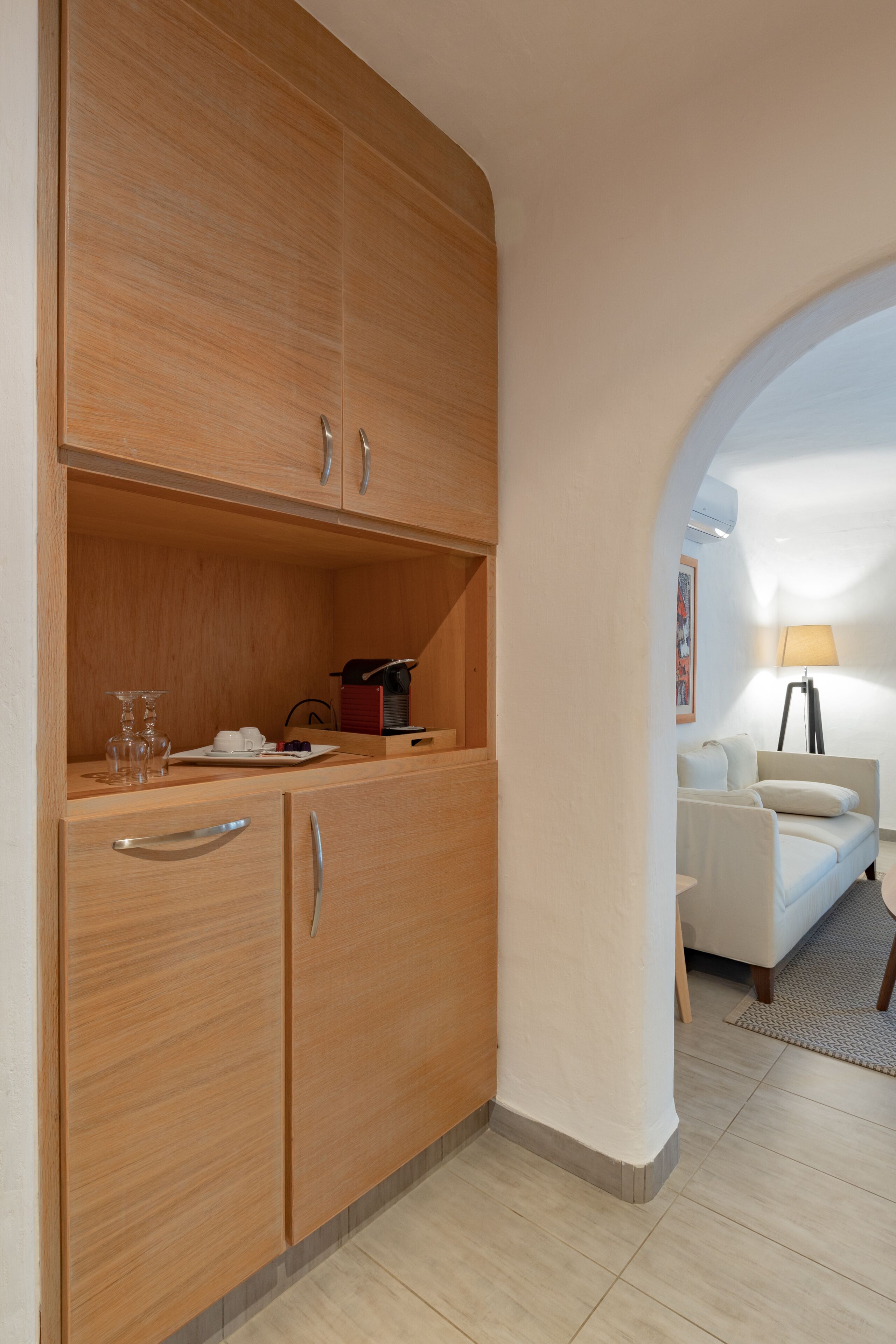A compact room with a wooden wardrobe, a small table with a lamp, and a white sofa.