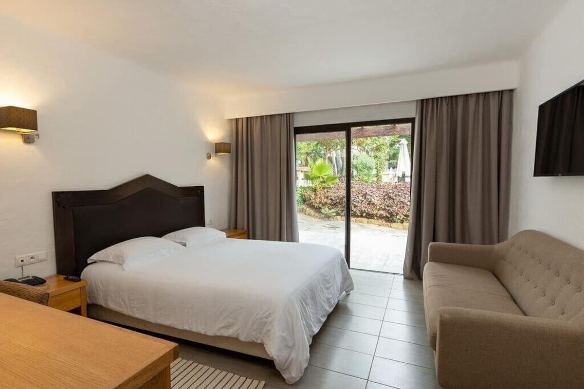 A hotel room with a bed, a desk, a chair, and a sliding glass door leading to an outdoor area.