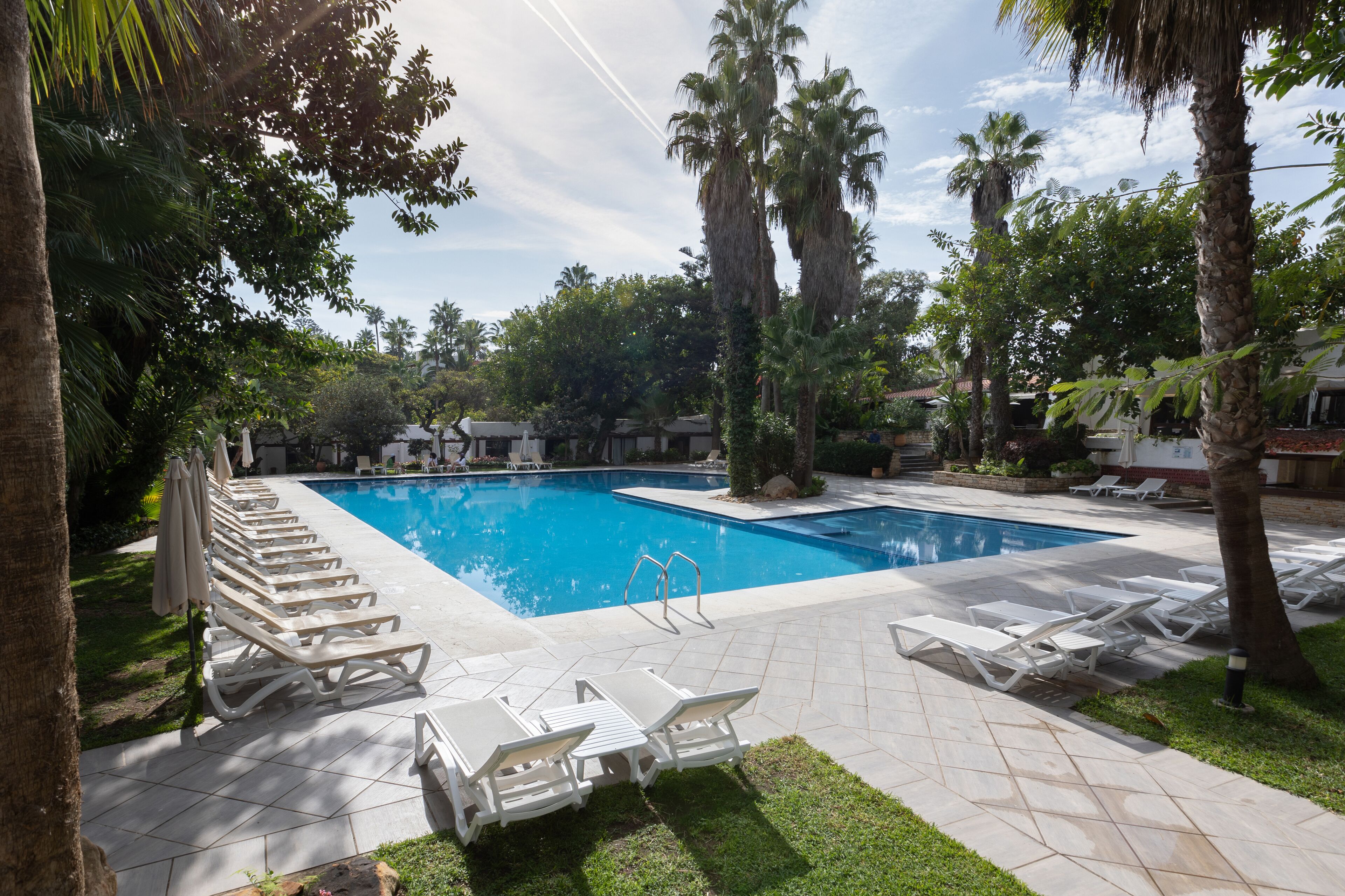 A swimming pool with lounge chairs and palm trees.
