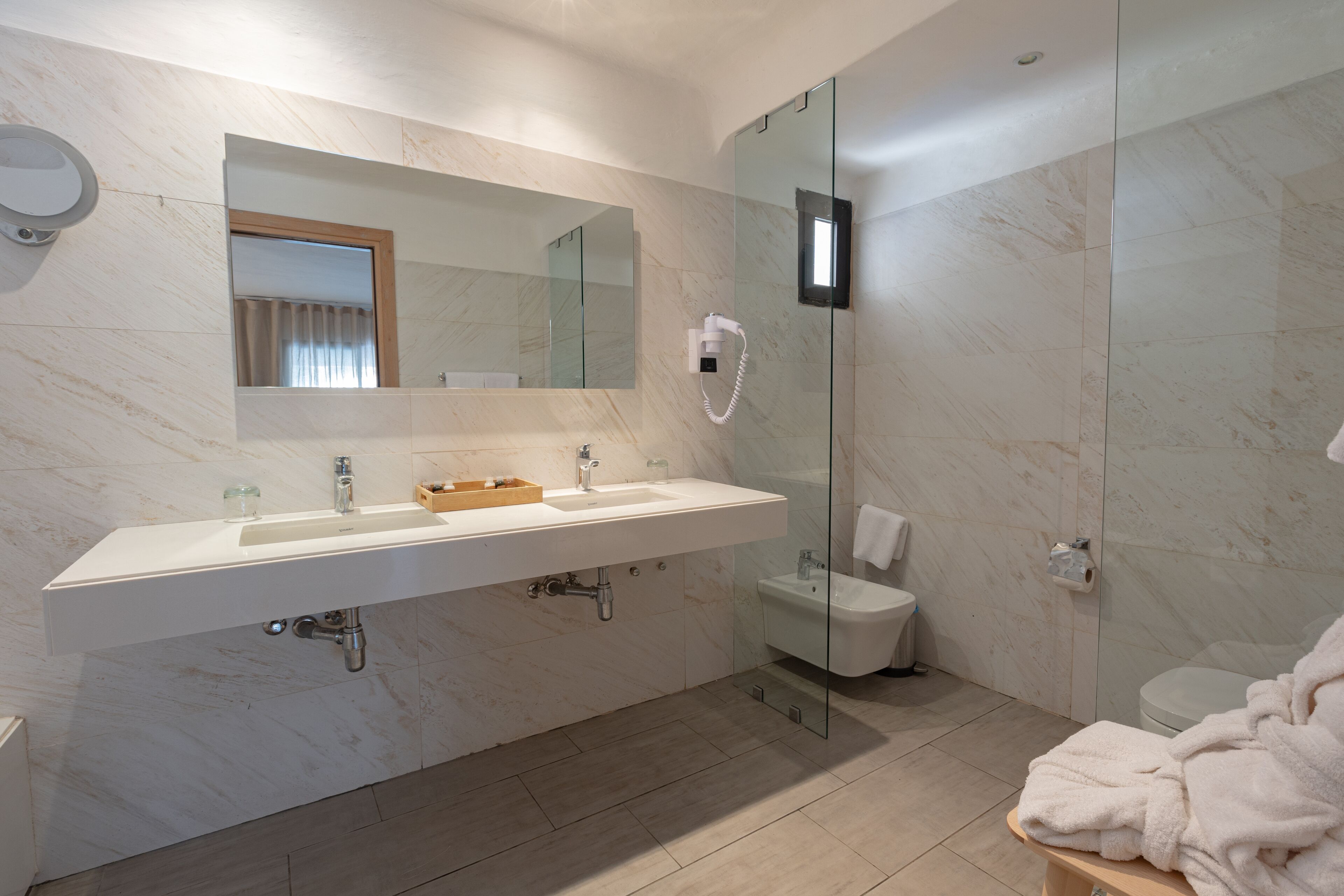 A modern bathroom with a large mirror, a sink, a bidet, and a glass shower enclosure.