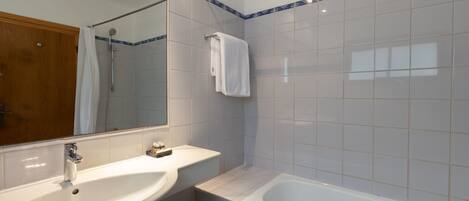 Un baño con lavamanos blanco, espejo, bañera y ducha.