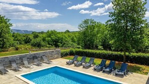 Une piscine rectangulaire bordée de pierres, entourée de chaises longues et d’un mur en pierre.