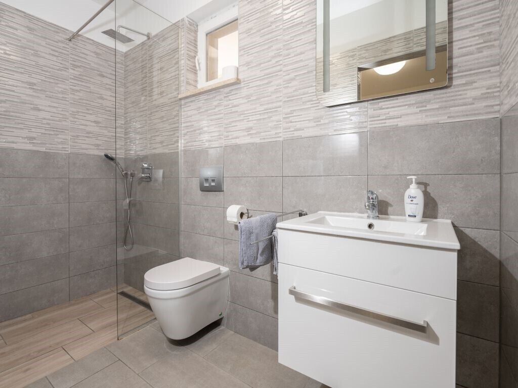 Ein modernes Badezimmer mit einer gläsernen Dusche, einer weißen Toilette und einem Waschtisch mit Waschbecken und Seifenspender.