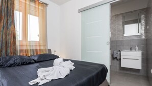 Une chambre d’hôtel moderne dotée d’un grand lit, d’une salle de bain avec un miroir et un lavabo, et d’une porte coulissante donnant accès à la salle de bain.