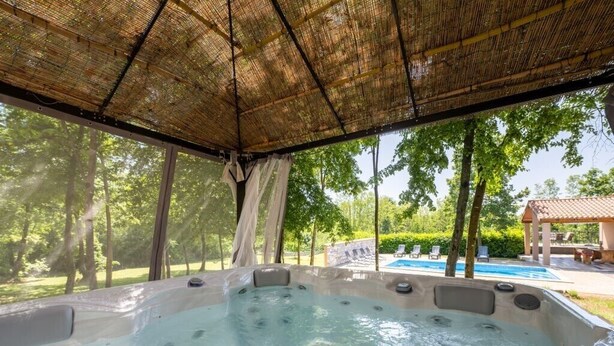 Un bain à remous doté d’un toit en bambou, entouré d’arbres, avec une piscine en arrière-plan.