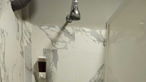 Une douche avec des carreaux de marbre et un pommeau de douche amovible.