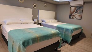 Une chambre d’hôtel avec deux lits, chacun recouvert d’une couverture turquoise, un grand miroir et un appareil de climatisation fixé au mur.