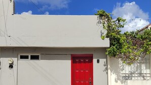 Un bâtiment avec une porte rouge, un mur blanc et un ciel bleu clair parsemé de nuages.
