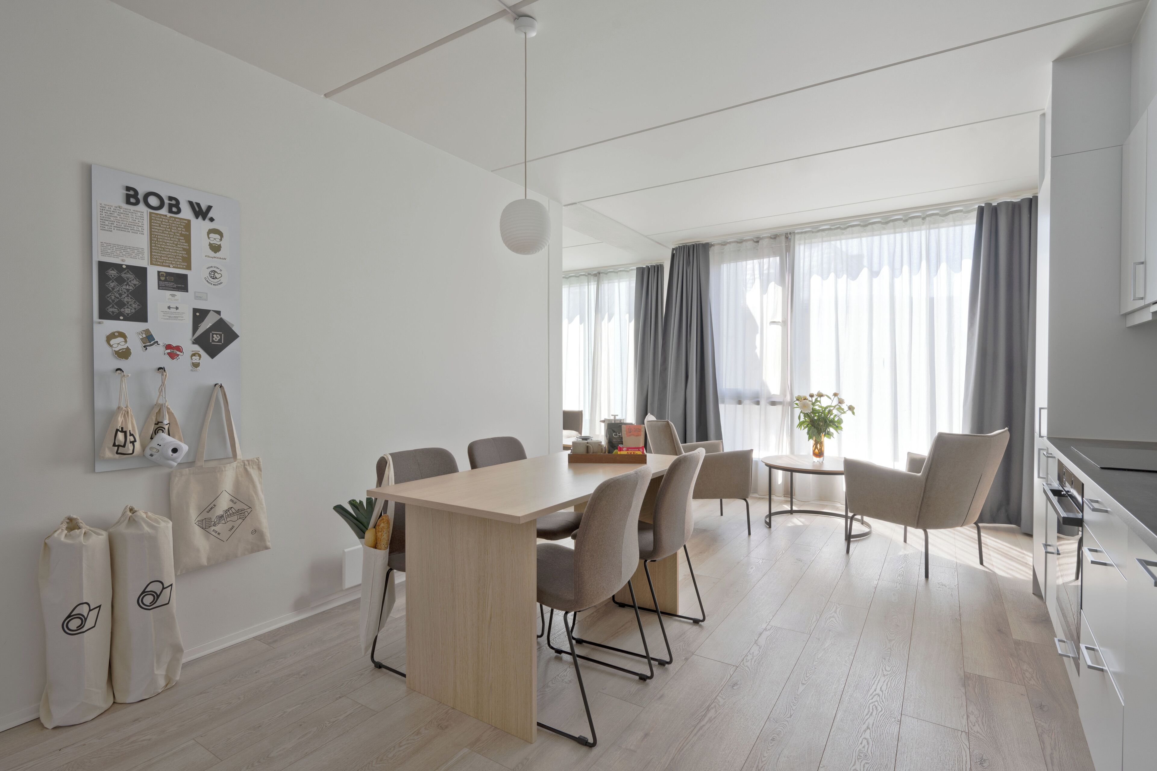 A modern, well-lit room with a wooden dining table, several chairs, a small side table, and a hanging light fixture.