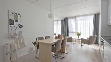 A modern, well-lit room with a wooden dining table, several chairs, a small side table, and a hanging light fixture.