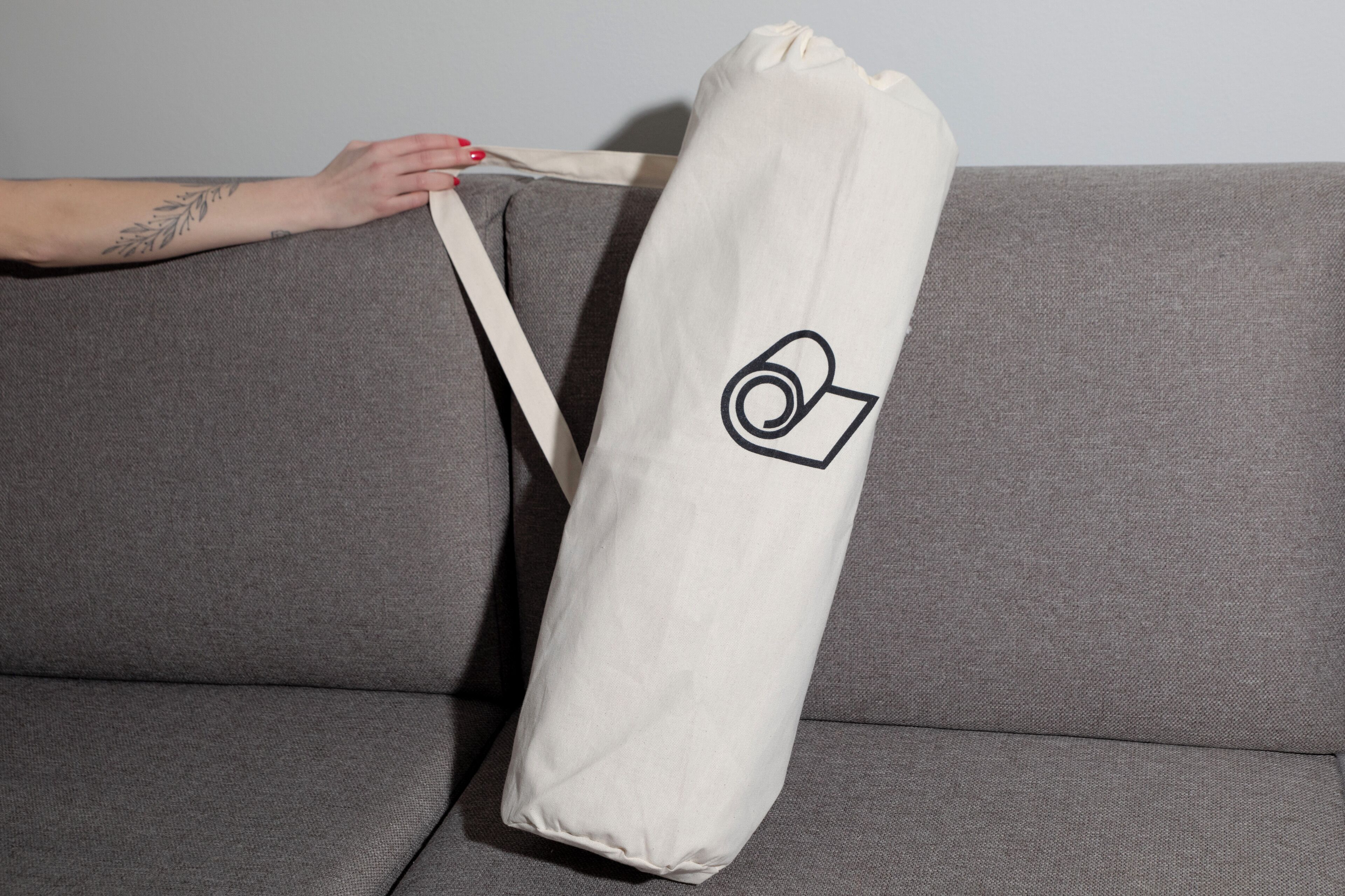 A grey sofa with a white bag featuring a black logo.