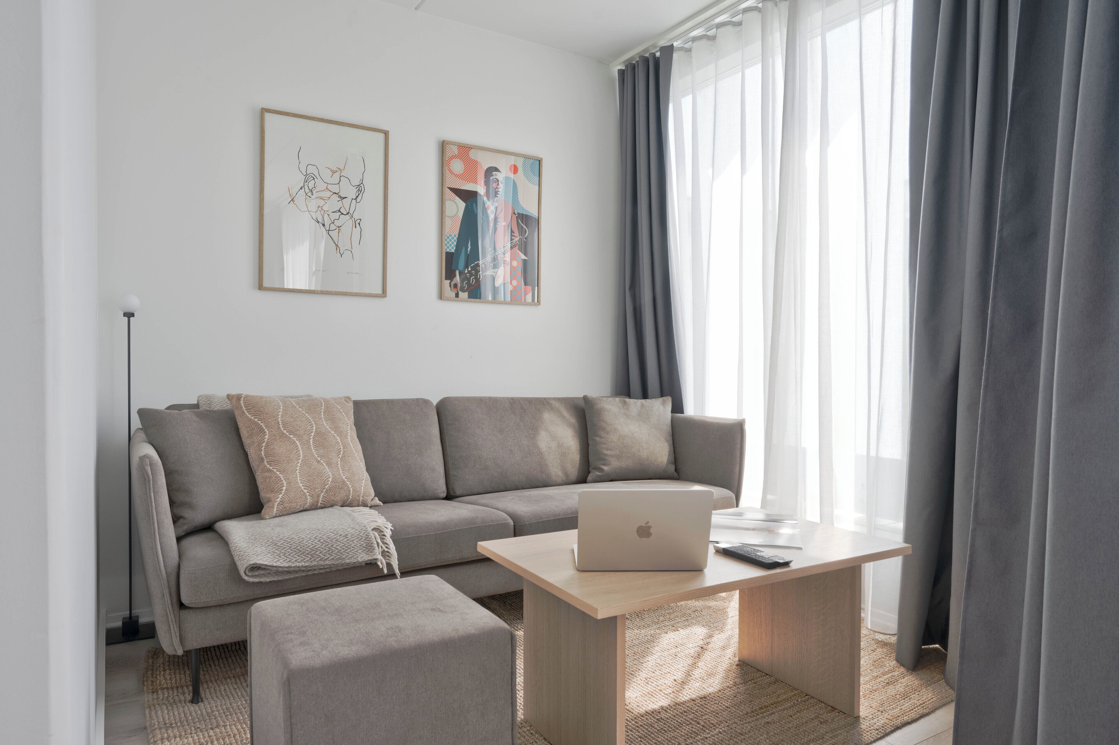 Un salon moderne avec un canapé gris, une table basse en bois sur laquelle se trouve un ordinateur portable, et des œuvres d’art accrochées au mur.