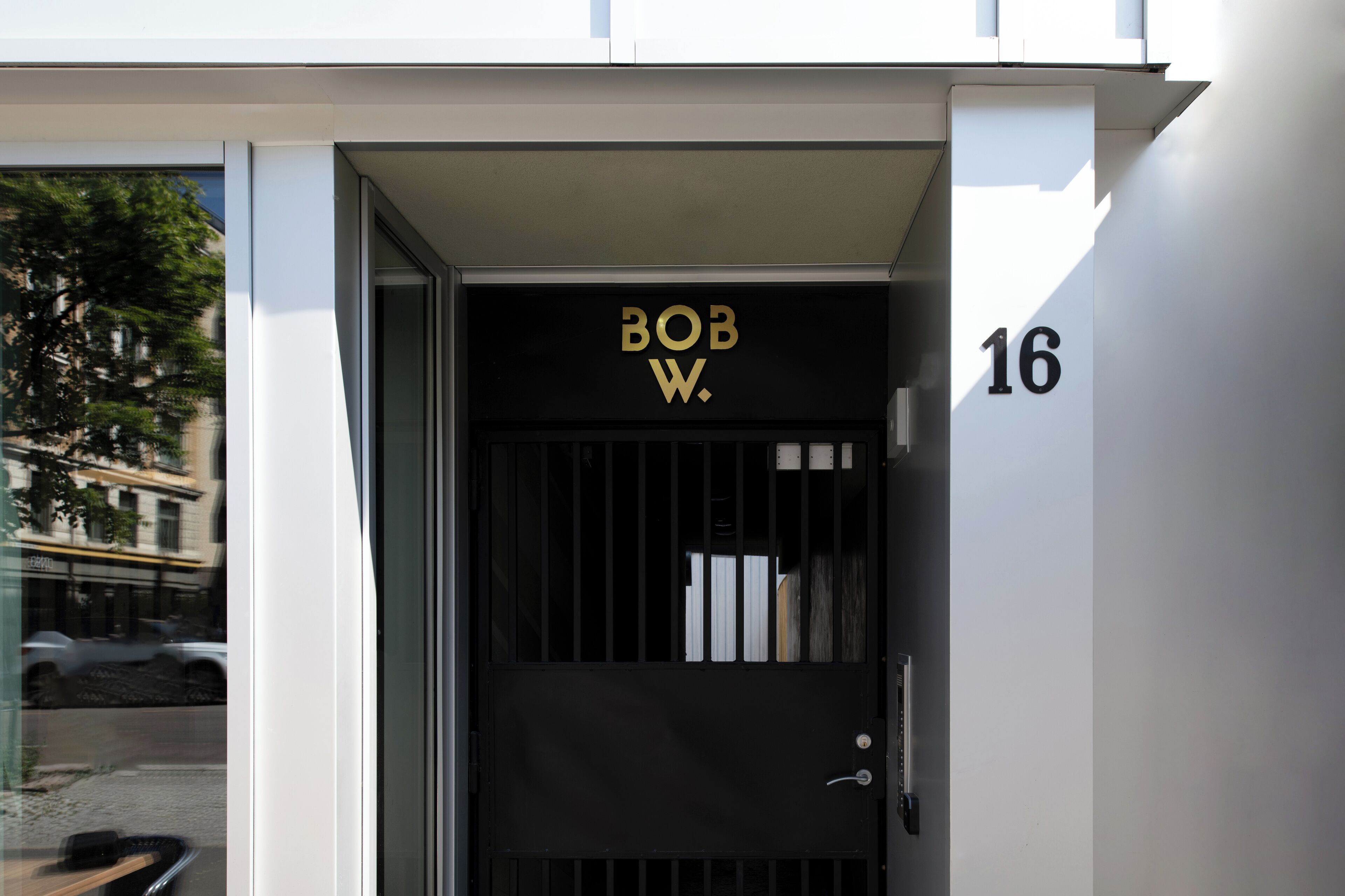 A modern building entrance with a black door labeled "BOB W." and the number "16" on the wall.