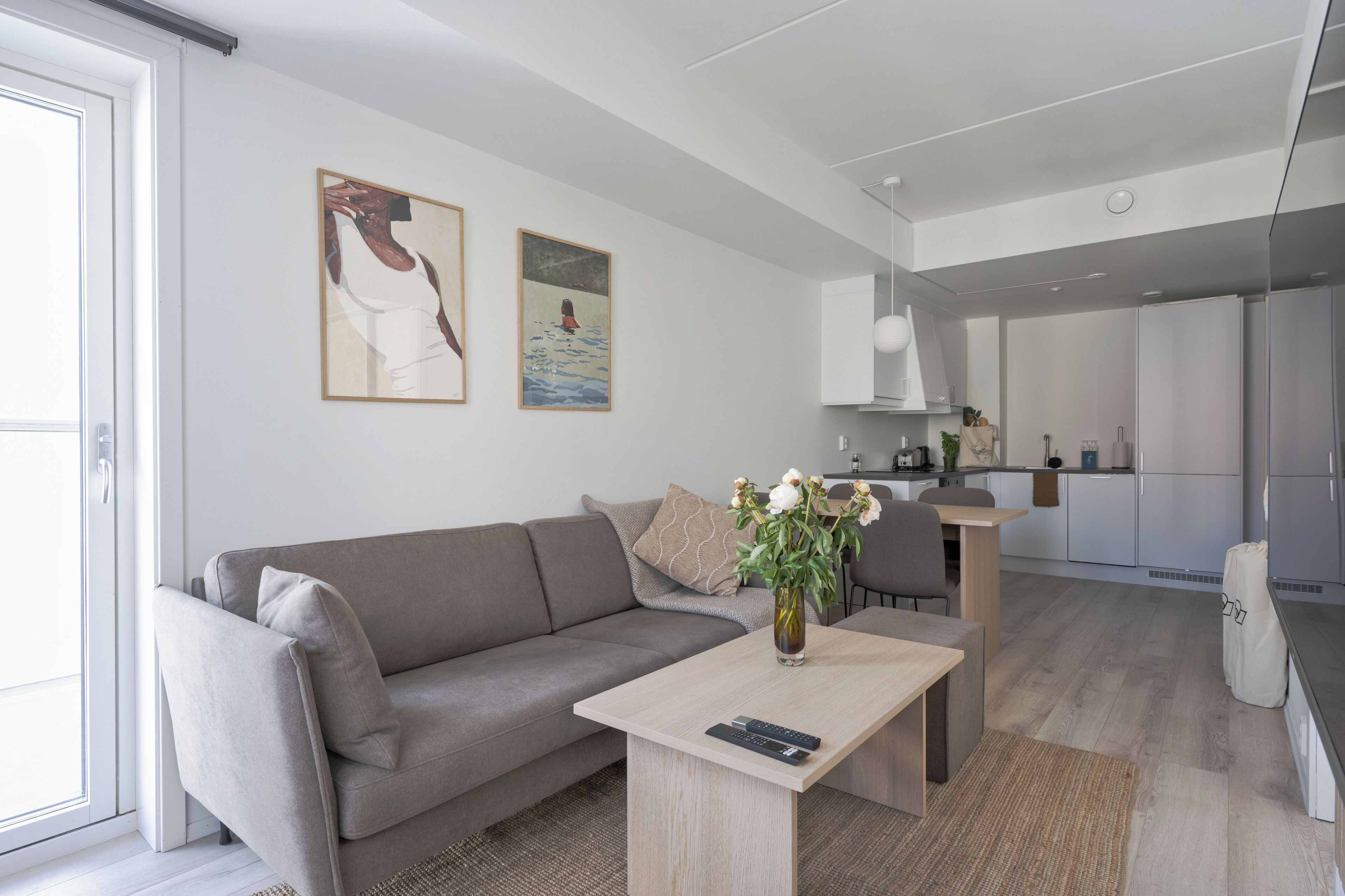 Un saló modern amb un sofà, una taula de centre amb un ram i una cuina al fons.
