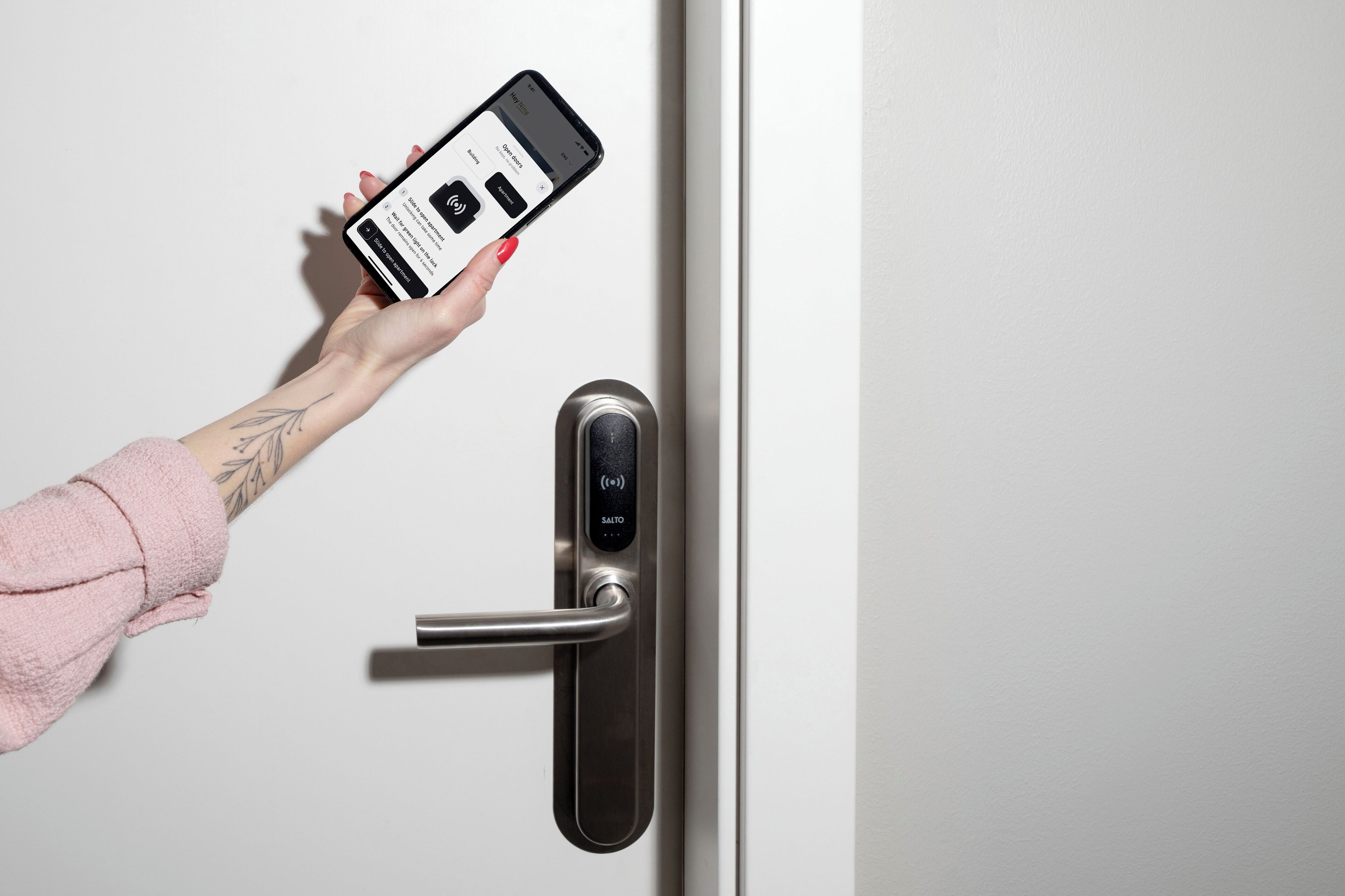 A hand holding a smartphone, interacting with a digital lock on a door.
