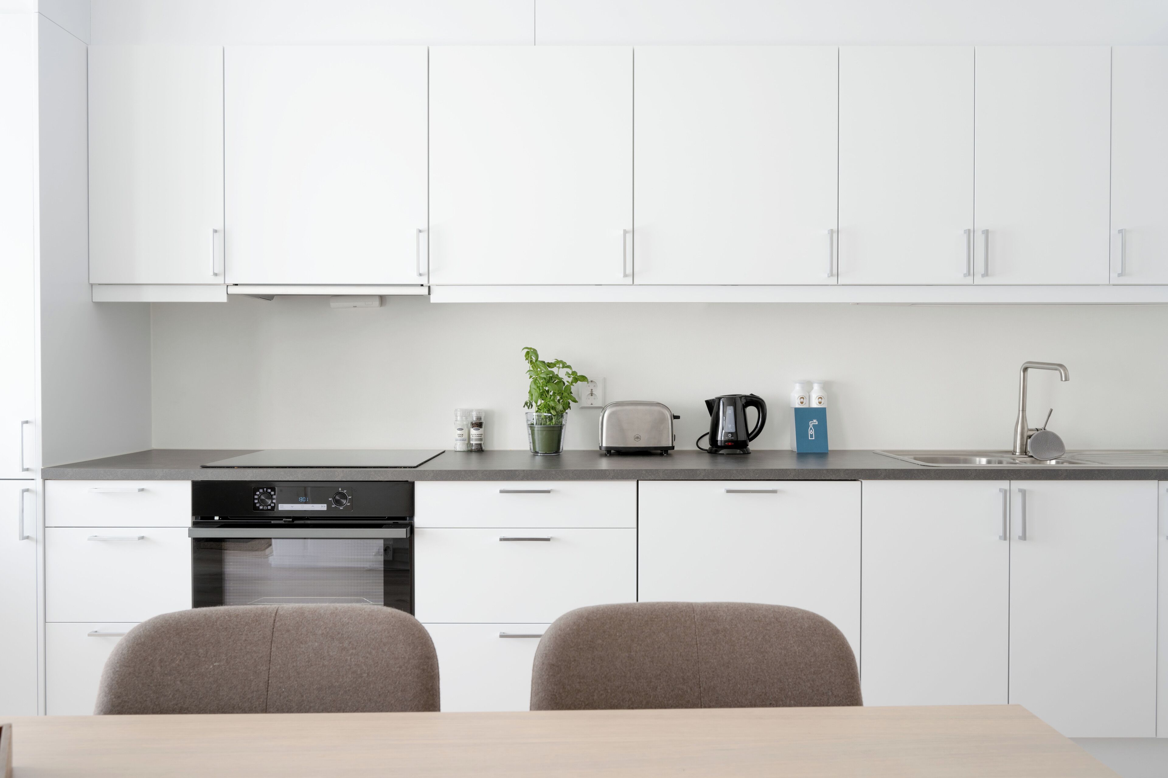 A modern kitchen with white cabinets, a black stove, a toaster, a kettle, and a sink.