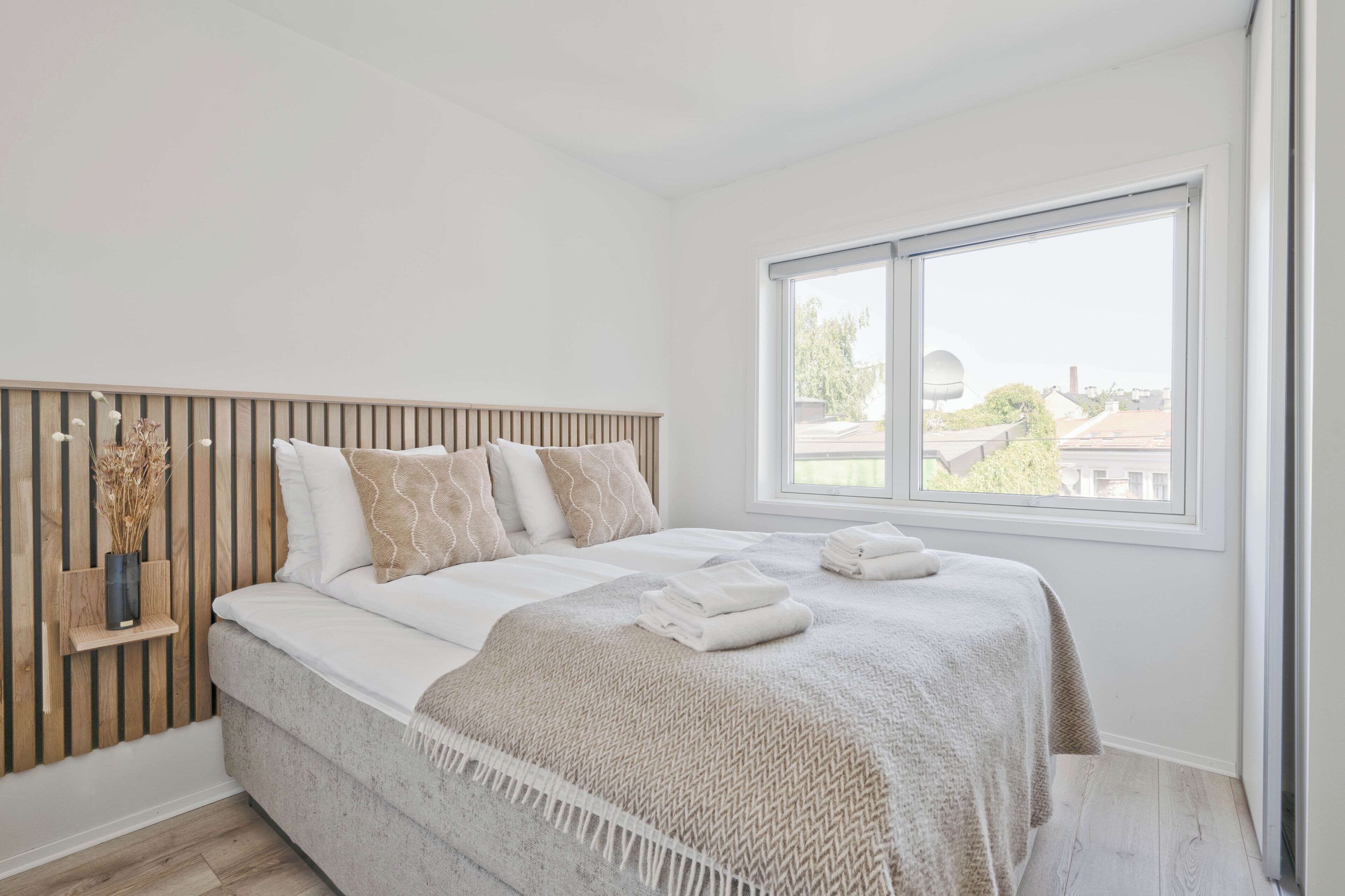 Een slaapkamer met een bed, een raam en een houten hoofdeinde.