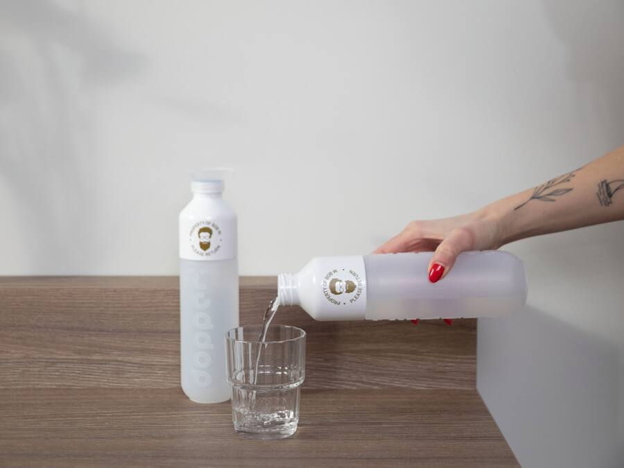 A hand pouring water from a bottle into a glass on a wooden table.