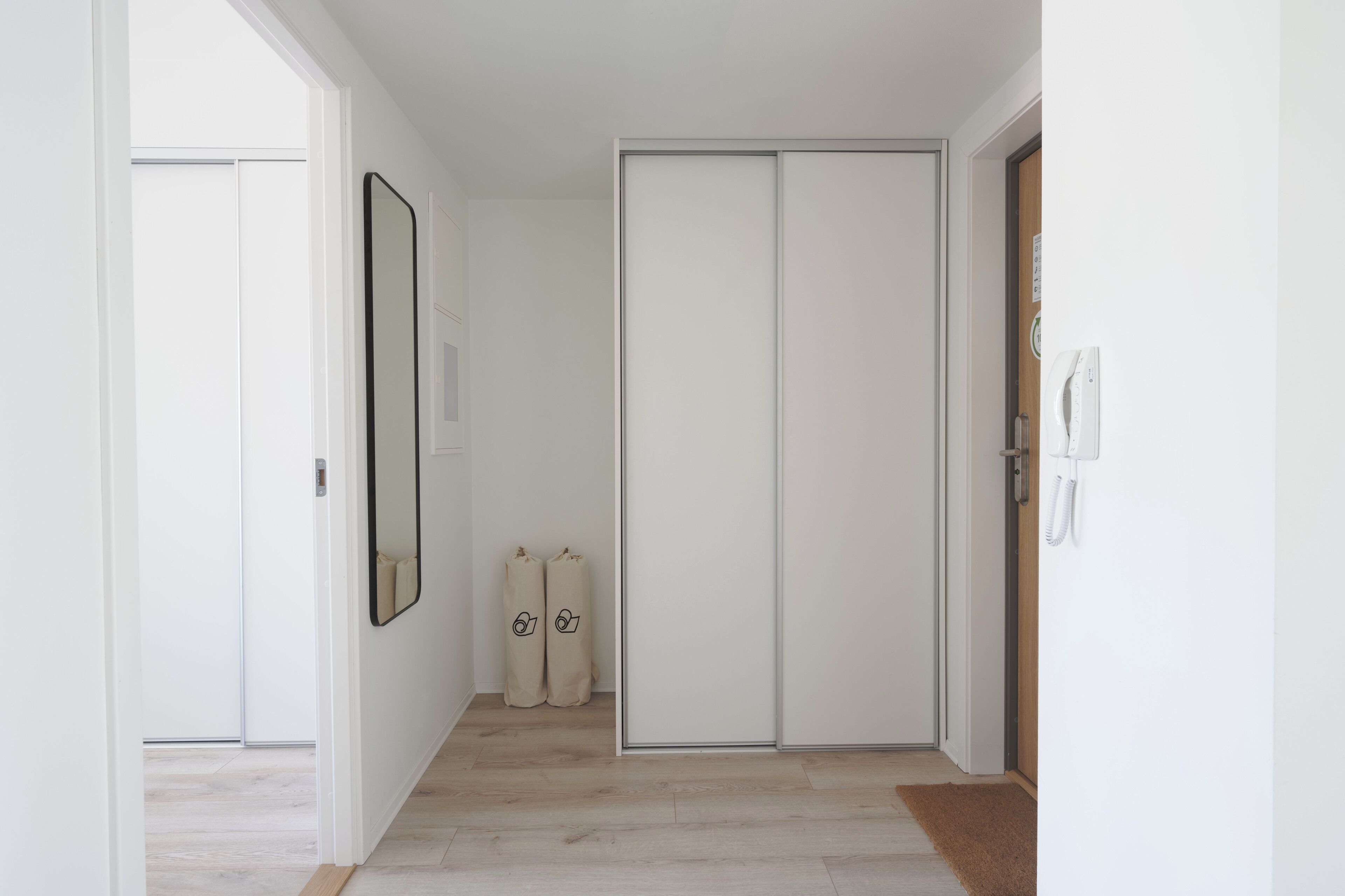 A hallway with a sliding door, a mirror, and two beige bags on the floor.