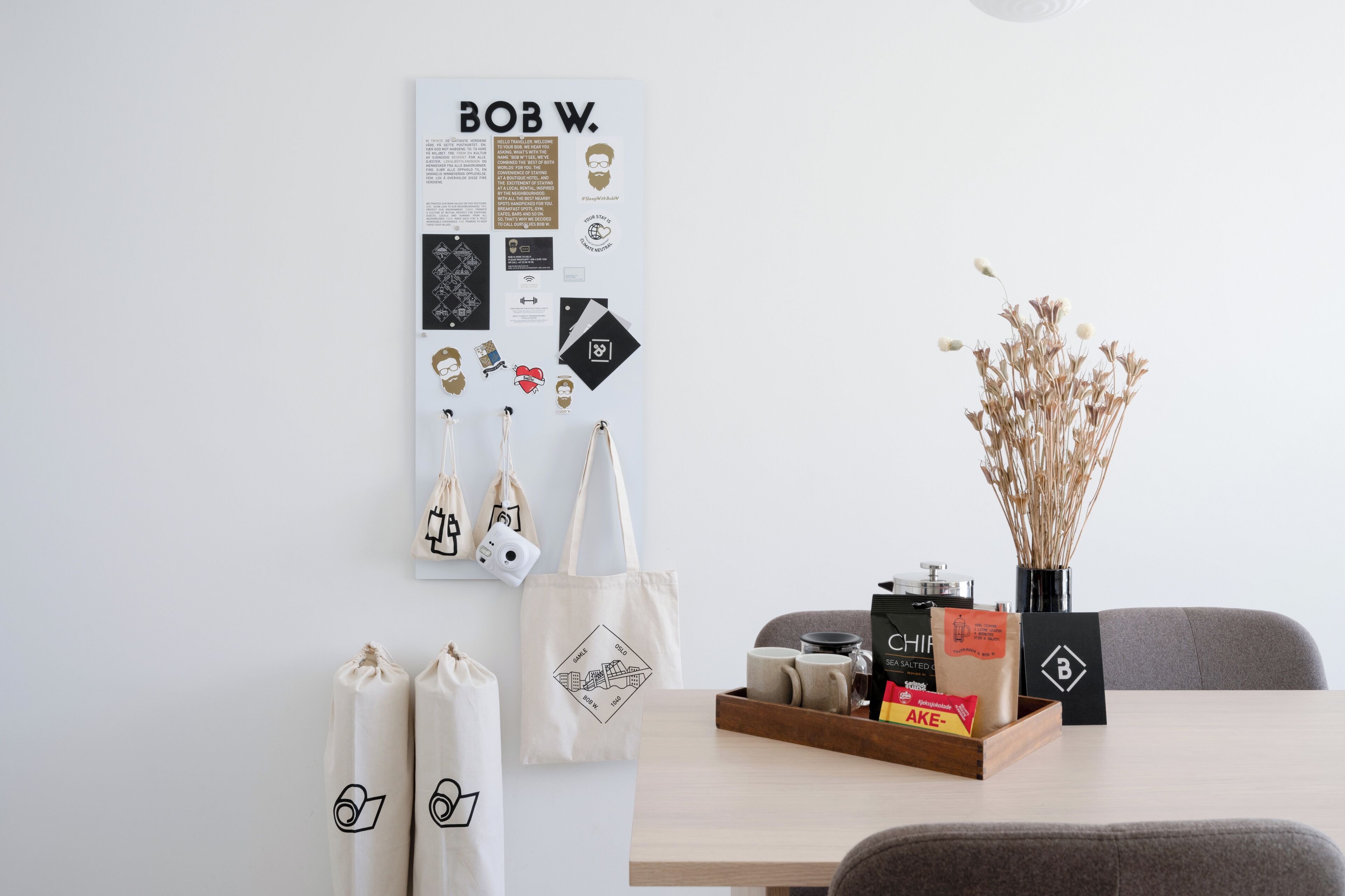 A wall with a poster, a table with a tray of items, and a vase with dried plants.