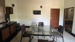 A dining area with a glass table, wicker chairs, a wooden ceiling, a kitchen area with a sink, and a door. - The Kingslayer Resort  (Negombo)