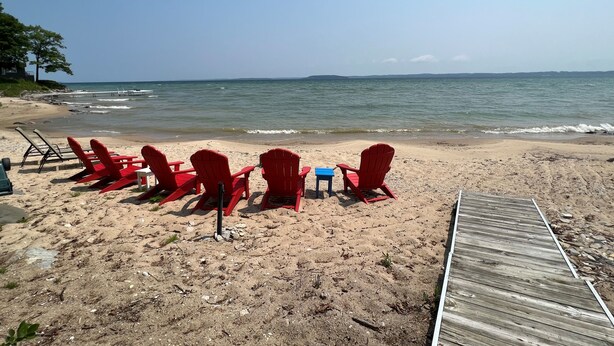 Une plage avec des chaises rouges et une petite table, une terrasse en bois et une vue dégagée sur l’océan.