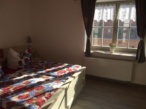 Une chambre à coucher avec un lit, une fenêtre avec des rideaux, un radiateur et une petite plante en pot sur le rebord de la fenêtre.