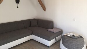 A modern, compact living space with a grey sectional sofa, a small grey bean bag, and a white wall with minimal decor.