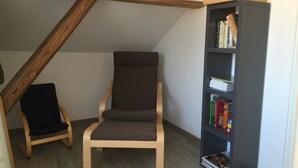A room with a wooden chair, a bookshelf, and a sloped ceiling.