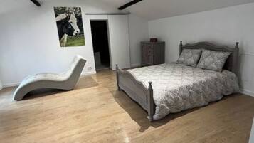 Un dormitorio con cama, una silla y suelo de madera.