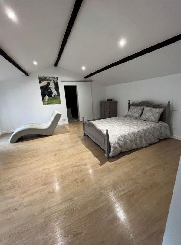 Quarto com uma cama, uma cadeira e piso de madeira.