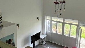 Ein großzügiger Wohnraum mit einem großen Fenster, einem roten Sofa, einem Glastisch und einem Fernseher.