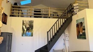 Ein geräumiger Wohnbereich mit hohen Decken, einer Holztreppe und einem Schlafzimmer im oberen Bereich.