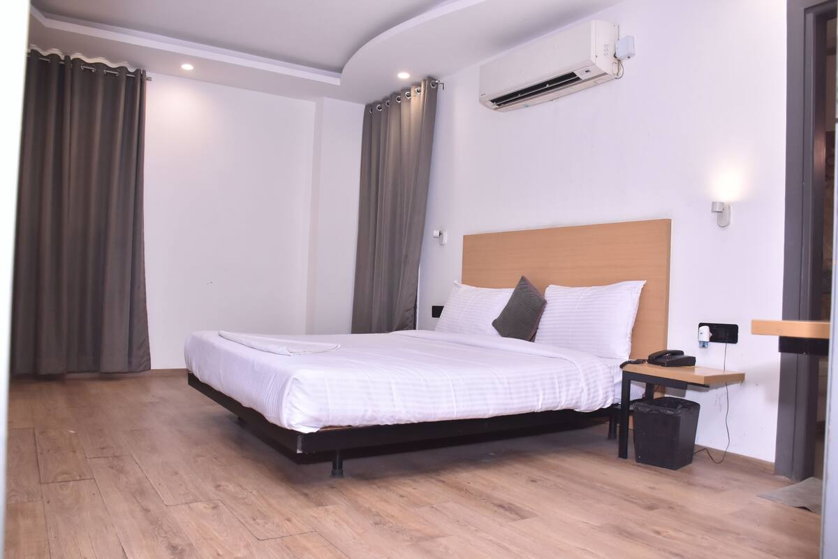 A hotel room with a bed, a desk, a chair, an air conditioning unit, and a wall-mounted phone.