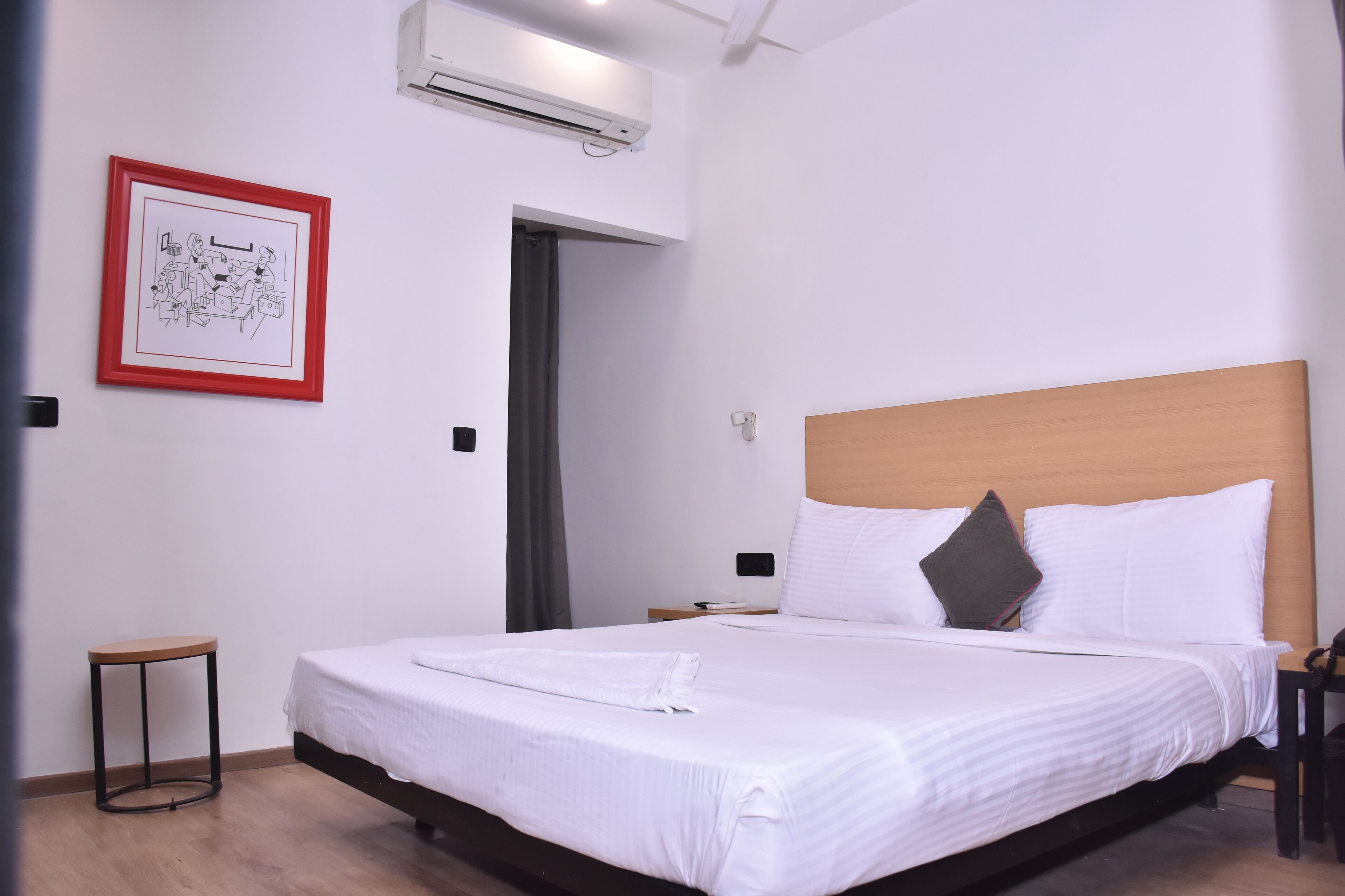 Een netjes opgemaakt bed met witte lakens en een houten hoofdbord, een klein nachtkastje en een lijst met een afbeelding aan de muur.