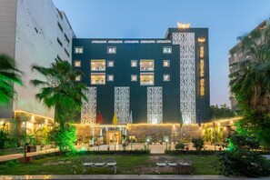 A multi-story hotel with a modern facade, balconies, and a well-lit entrance. - Chhavi Hotels (Noida)