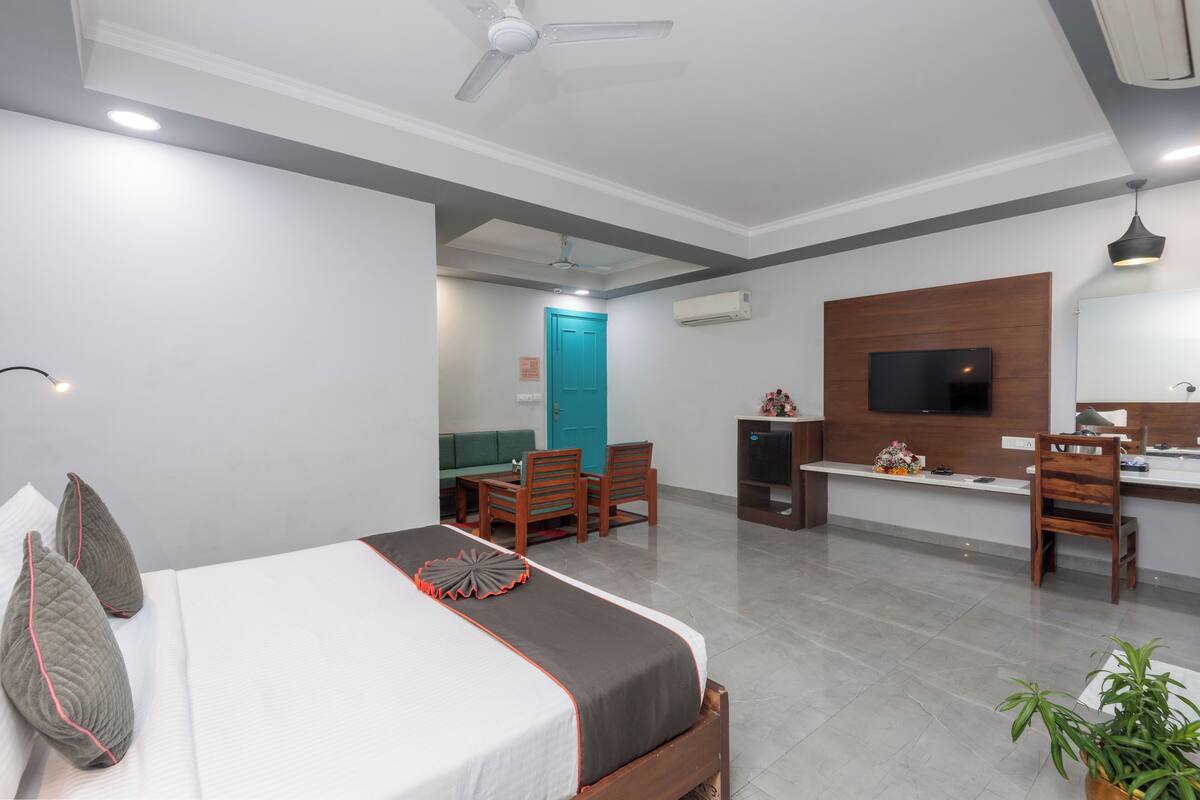 A hotel room with a bed, a desk, a TV, and a dining area.