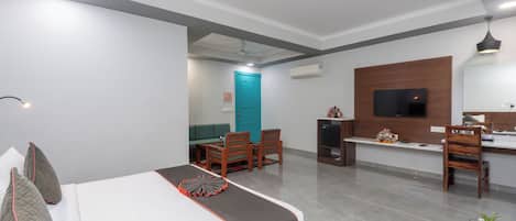 A hotel room with a bed, a desk, a TV, and a dining area.