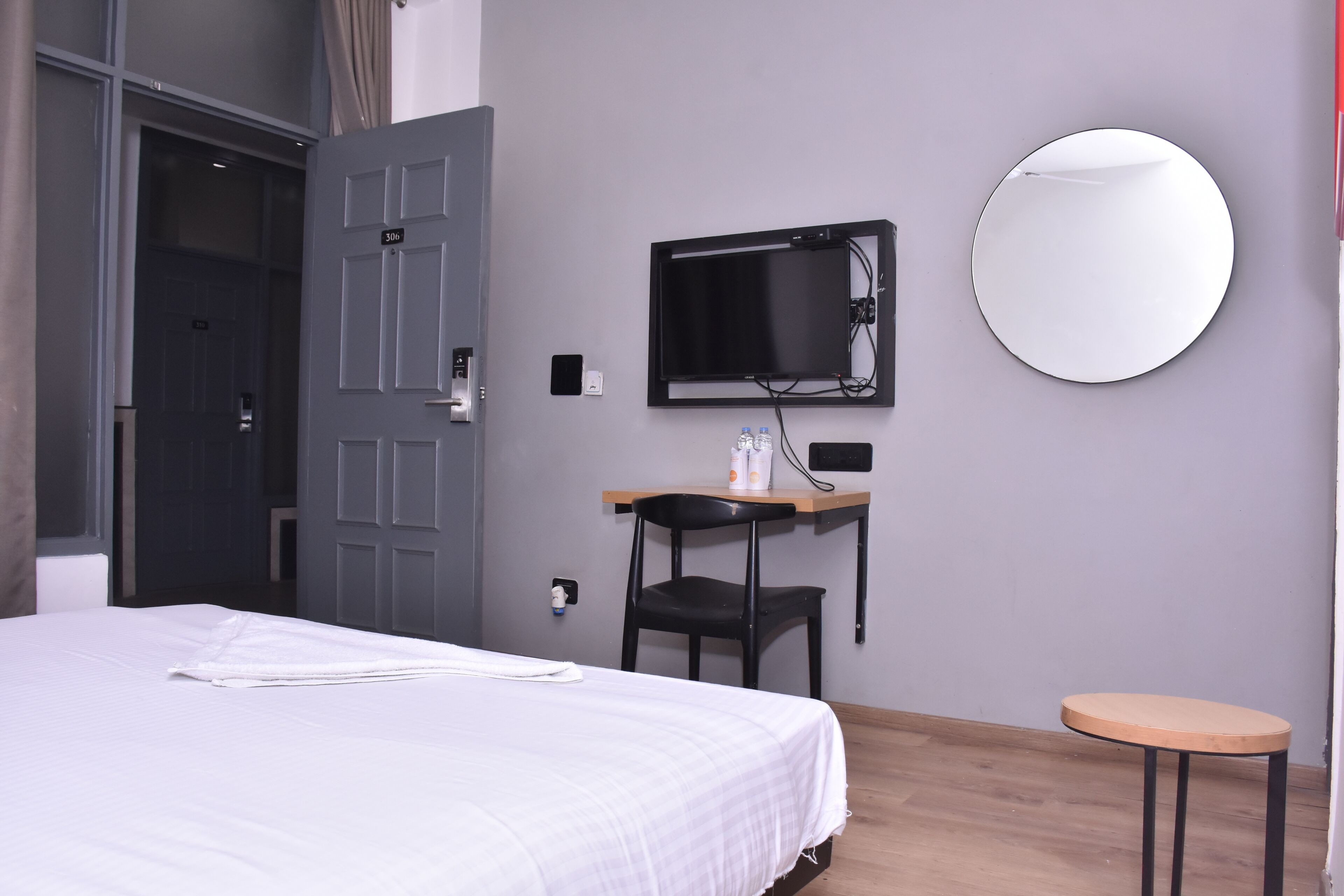 Een hotelkamer met een bed, een bureau met stoel, een televisie en een ronde spiegel aan de muur.
