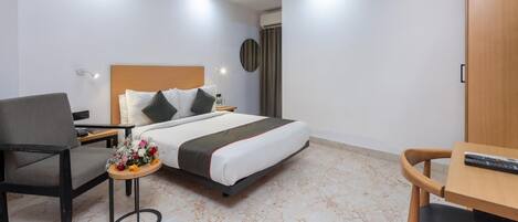 Habitación de hotel con cama, escritorio, silla, mesita con un jarrón de flores, ventilador de techo y televisor montado en la pared.