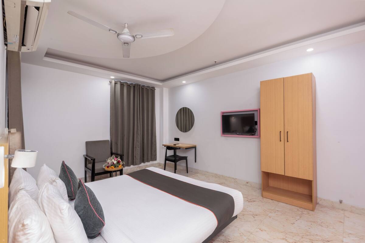 A hotel room with a bed, a desk, a chair, a wardrobe, a ceiling fan, and a TV mounted on the wall.